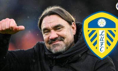 Leeds United manager Daniel Farke holding a thumbs up and smiling next to a Leeds badge.